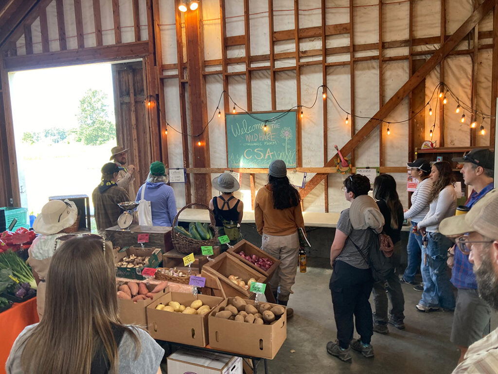 A group of people in a barn looking up at a chalkboard that has information about a CSA written on it