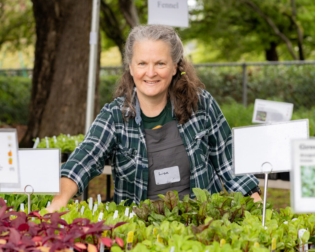 A smiling volunteer tends to rows of leafy greens and vegetables at the Edible Plant Sale.